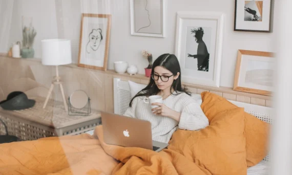 Woman relaxing in bed with a warm comforter while working on laptop